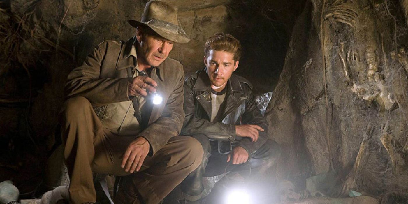 Индиана Джонс и Матт Уильямс исследуют что-то на земле в пещере с фонариками.